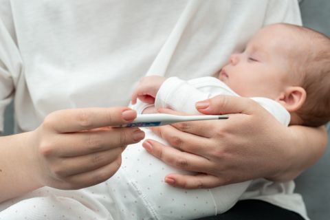 mamma con termometro in mano e neonato con febbre